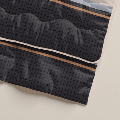 Eine Nahaufnahme des dunklen, gesteppten Stoffes mit Gittermuster und dünnen beigen und braunen Streifen entlang der Ränder, gelegt auf eine helle Oberfläche - ideal als antiallergische Bettdecke wie das Zelesta Royalbed - Blue Stripes.