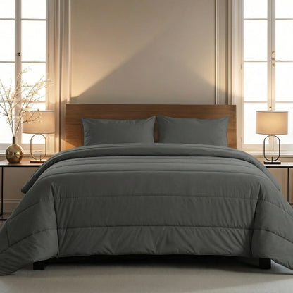Ein ordentlich gemachtes Bett mit einer grauen Bettdecke und Zelesta Comfort Uni Kissenbezüge Set von 2 - Anthrazit in 80x80cm, Holzkopfteil, zwei Nachttische mit Lampen und zwei Fenster im Hintergrund.