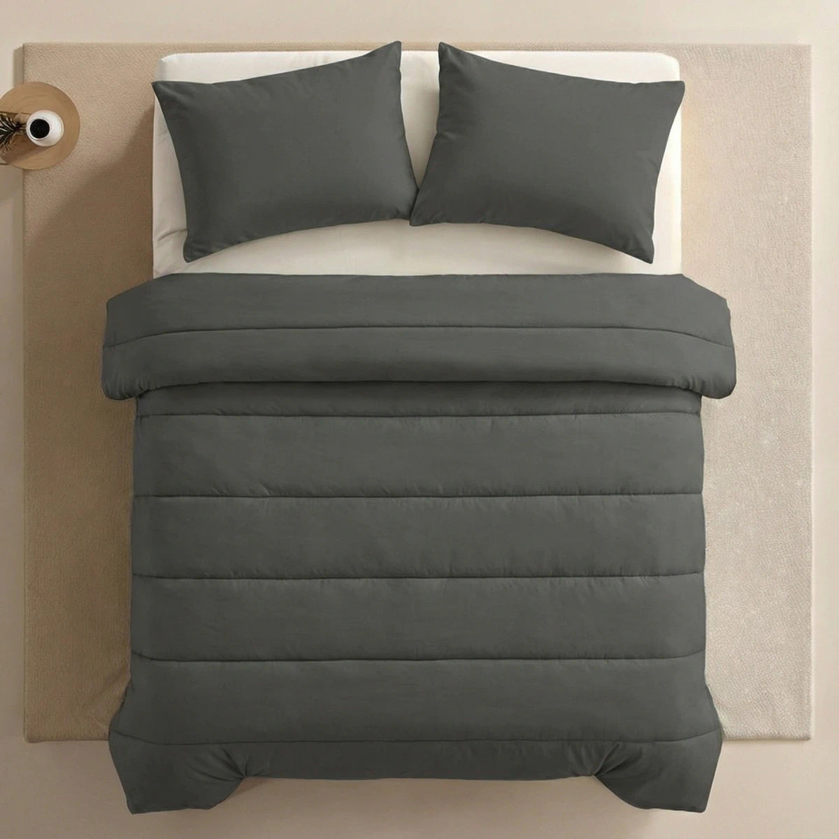 Ein ordentlich gemachtes Bett mit einer dunkelgrauen Bettdecke und zwei passenden Zelesta Comfort Uni Kissenbezügen Set von 2 in Anthrazit (80x80cm) auf einem hellen Teppich, von oben gesehen.