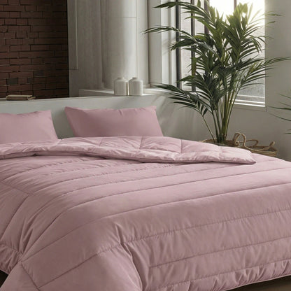 Ein ordentlich gemachtes Bett mit einer Zelesta Comfort Uni Bettdecke in altrosa und passenden Kissen steht in einem modernen Schlafzimmer mit großen Fenstern, einer Backsteinwand und einer hohen Grünpflanze.