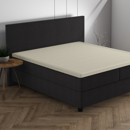Ein minimalistisches Schlafzimmer mit einem dunklen Polsterbett, Doppel Jersey Topper Spannbettlaken - Creme, einem runden Beistelltisch aus Holz, einer kleinen Pflanze und einem Holzboden mit Fischgrätmuster - perfekt für Ihr Traumhaus.