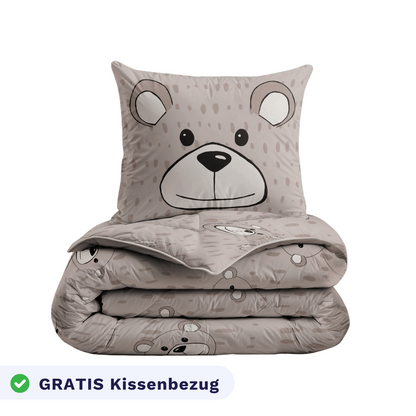 Das gefaltete Zelesta Kiddybed - Happy Bear Set zeigt ein beiges Bärengesicht, enthält ein passendes Kissen und eine Bettdecke, ist hypoallergen und ideal für Kinderbetten. Ein Etikett an der Unterseite lautet GRATIS Kissenbezug.