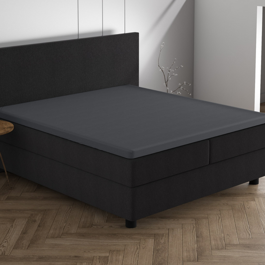 Ein modernes Schlafzimmer mit einem schwarzen Bett mit dem Doppel Jersey Topper Spannbettlaken - Grau auf einem Holzfußboden und minimalem Dekor, das eine echte Dreamhouse-Atmosphäre schafft.