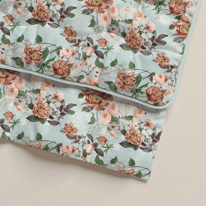 Zwei gefaltete Zelesta Royalbed - Happy Flower Bettdecken in hellblau mit rosa und roten Rosen, grünen Blättern und kleinen Zweigen. Gefertigt aus Mikrofaser Bettdecke, perfekt als antiallergische Bettdecke auf einem neutralen Hintergrund.