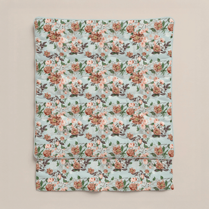 Eine gefaltete Zelesta Royalbed - Happy Flower Mikrofaser Bettdecke in Hellblau mit einem sich wiederholenden floralen Muster aus rosa, burgunderroten und weißen Blüten sowie grünen Blättern auf neutralem Hintergrund.