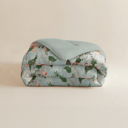 Eine sauber gefaltete Zelesta Royalbed - Happy Flower Mikrofaser Bettdecke mit einem hellblauen Oberteil und einem floralen Muster aus grünen Blättern und rosa Blüten.