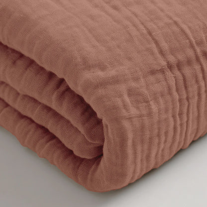 Ein gefaltetes Musselin Spannbettlaken - Dusty-Rose mit einer strukturierten Oberfläche ist in Nahaufnahme auf einer weißen Fläche zu sehen.