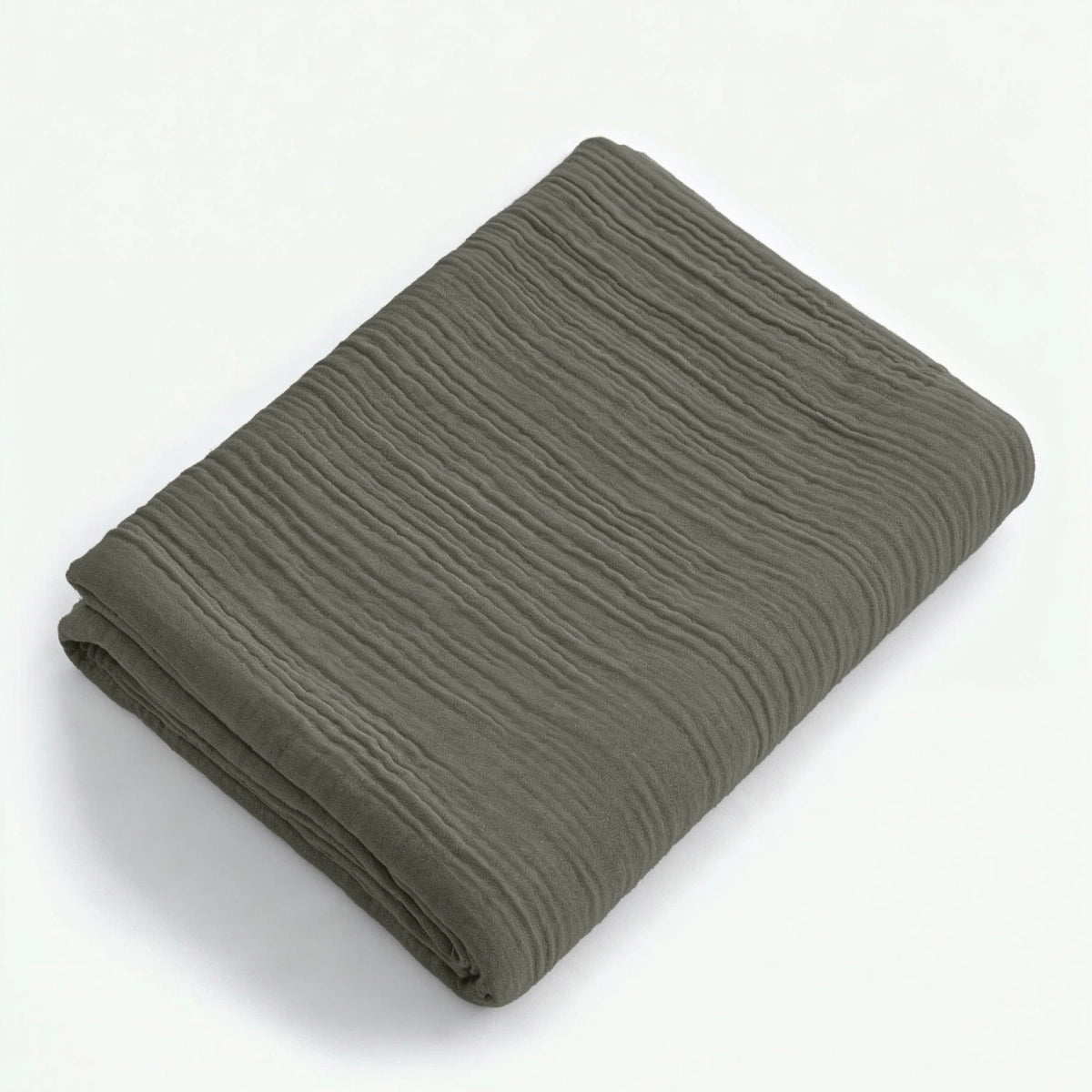 Ein sauber gefaltetes Musselin Spannbettlaken in Graugrün mit strukturierter Oberfläche und minimalistischem Japandi-Stil wird auf einer schlichten weißen Fläche präsentiert.