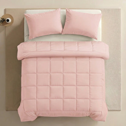 Ein ordentlich gemachtes Bett mit der Zelesta Pure Uni Bettdecke - Zartrosa, einer hellrosa Steppdecke mit zwei passenden Kissen auf einer beigen Oberfläche, betont den ganzjährigen Komfort und den gemütlichen Stil.