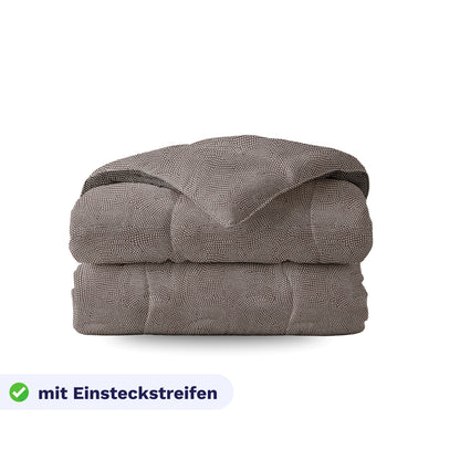 Gefaltete Royalbed Baumwolle - Brown Animal Bettdecke mit braunem Tiermuster und strukturierter Oberfläche, abgebildet auf weißem Hintergrund. Auf dem Etikett steht "mit Einsteckstreifen" mit grünem Karomuster - ideal als Baumwollbettdecke und für Allergiker geeignet.