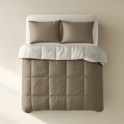 Ein gemachtes Bett mit zwei braunen Kissen und einer taupefarbenen Bettdecke aus dem Zelesta Premiumbed Baumwolle - Taupe & Cream, bedeckt mit einer gefalteten hellgrauen Decke, von oben gesehen vor einem beigen Hintergrund.