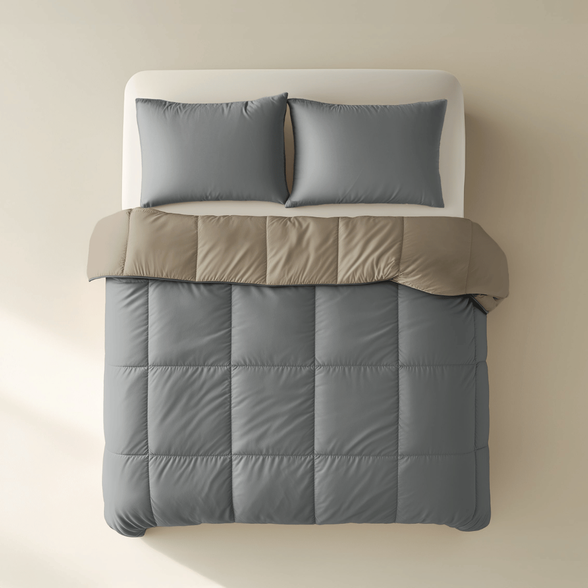 Ein ordentlich gemachtes Bett mit der Zelesta Premiumbed Baumwolle in Anthrazit & Taupe und zwei passenden Kissen, von oben gesehen auf einem hellbeigen Hintergrund.
