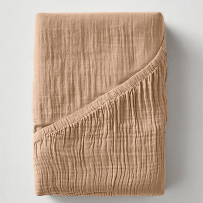 Gefaltete Musselin-Spannbettlaken - Terra in Beige, mit einer leicht geknitterten Struktur und einer umgeschlagenen Ecke, die die Innenseite zeigt.