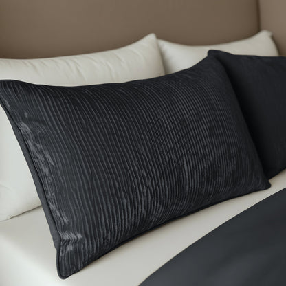 Zwei anthrazitfarbene Zelesta Velvetbed Chique Kissenbezüge liegen auf einem weißen Bett, mit einem beigen Kopfteil im Hintergrund.