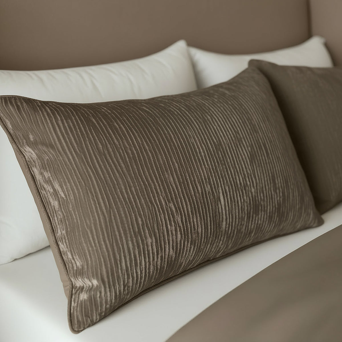 Eine Nahaufnahme des Zelesta Velvetbed Chique Kissenbezüge Set von 2 in Taupe, mit strukturierten Bezügen auf einem passenden Samtbett mit weißen Laken und koordinierter taupefarbener Bettwäsche aus hochwertigem Stoff.