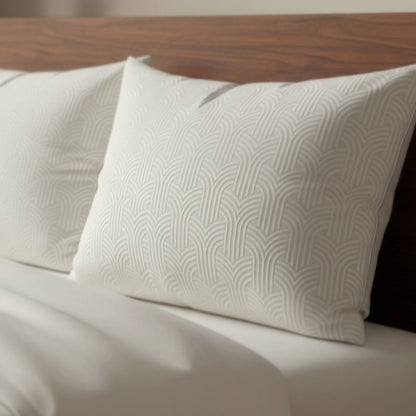Zwei cremefarbene Zelesta Flanel Art Kissenbezüge (Set von 2, 80x80cm) mit dezentem geometrischen Muster liegen auf einem ordentlich gemachten Bett mit weißen Laken und lehnen an einem hölzernen Kopfteil.