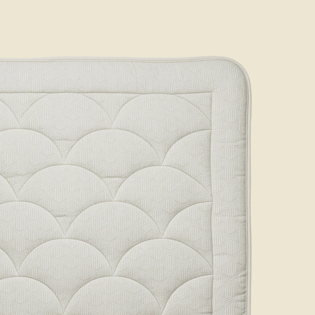 Nahaufnahme der Ecke der Zelesta Flanel Luxe - Creme Matratze mit strukturiertem, muschelgemustertem Stoff auf hellbeigem Hintergrund, ideal zur Kombination mit einer temperaturregulierenden Bettdecke.
