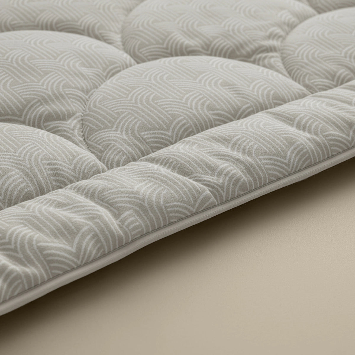 Nahaufnahme der Zelesta Flanel Luxe - Taupe & Grey Matratzenauflage mit Polsterung, Temperaturregulierung und einem hellgrauen geometrischen Muster auf beiger Oberfläche.