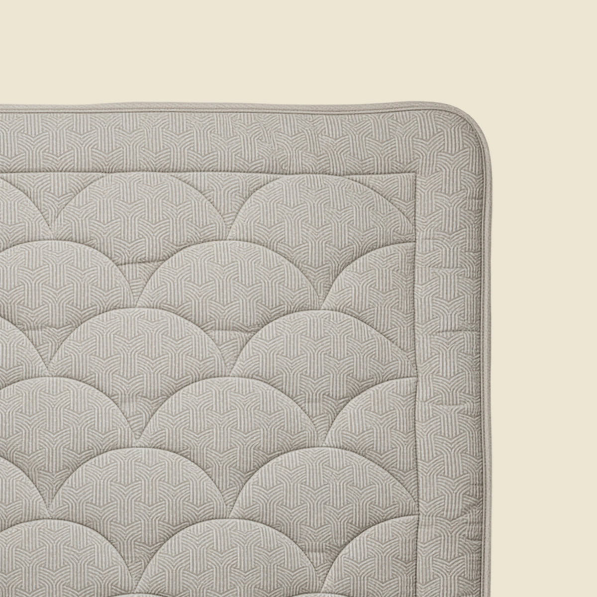 Eine Nahaufnahme der Ecke einer Zelesta Flanel Luxe - Taupe & Grey Matratze zeigt die hellgraue, temperaturregulierende Oberfläche mit einem geometrischen, sich wiederholenden Muster auf einer beigen Unterlage.