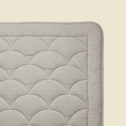 Eine Nahaufnahme der Ecke einer Zelesta Flanel Luxe - Taupe & Grey Matratze zeigt die hellgraue, temperaturregulierende Oberfläche mit einem geometrischen, sich wiederholenden Muster auf einer beigen Unterlage.