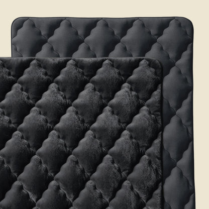 Zelesta Flanel Uni - Schwarz: Zwei überlappende schwarze Steppmatten - eine mit samtartigem Rautenmuster, die andere glatt - vor beigem Hintergrund, perfekt als ganzjährig temperaturregulierende Mikrofaser oder Flanel Bettdecke.