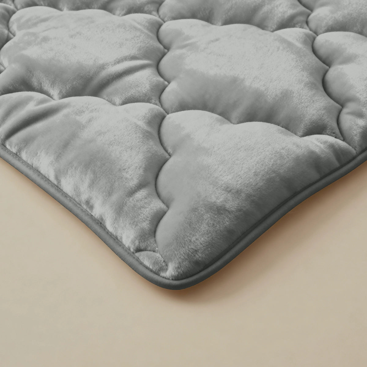 Nahaufnahme der Zelesta Flanel Uni - Khaki Matratzenauflage mit einer grauen, gesteppten, samtigen Oberfläche und wolkenartigem Muster auf beige-perfekt für extra Weichheit und temperaturregulierenden Komfort.