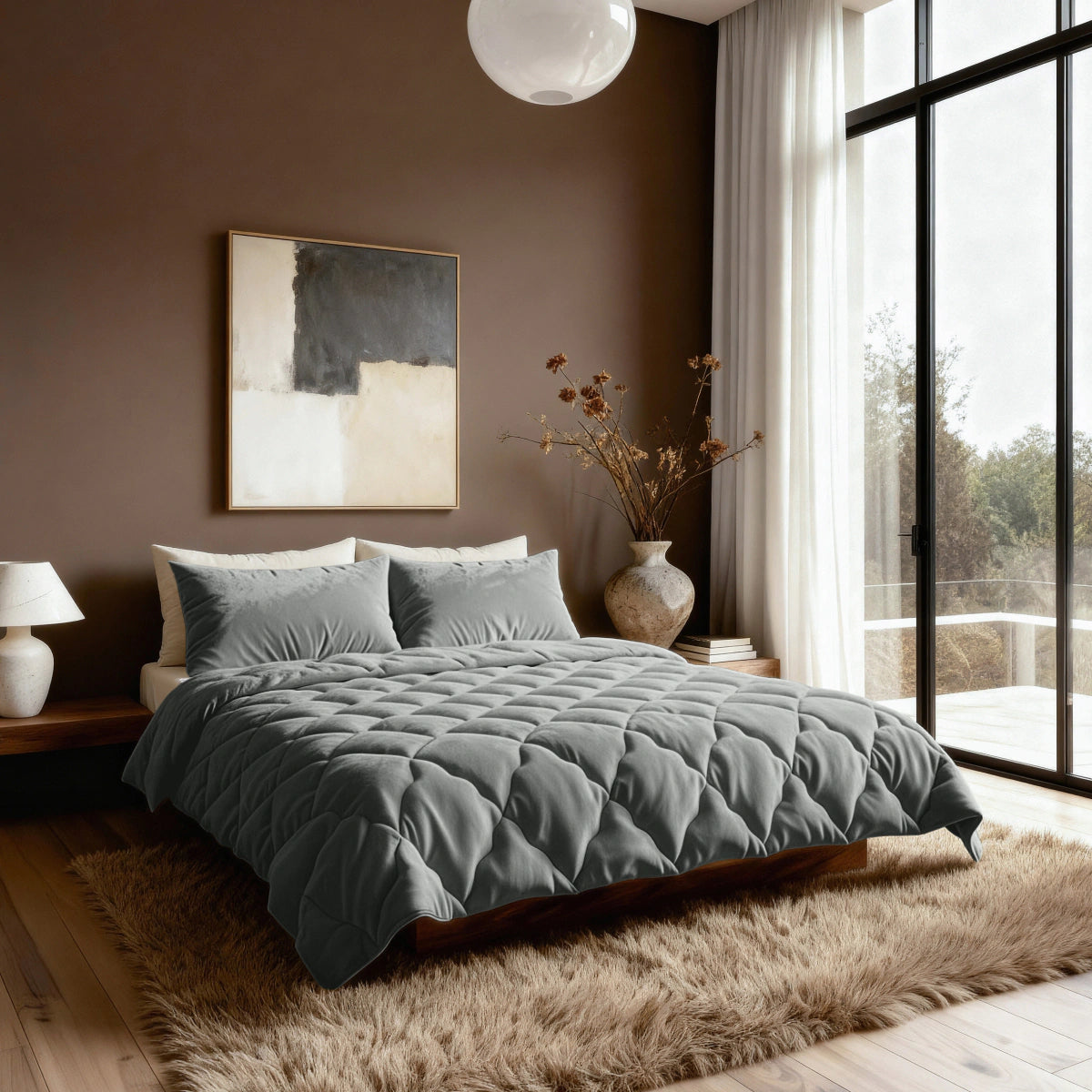 Ein modernes Schlafzimmer mit einem großen Bett, einer khakifarbenen Bettdecke von Zelesta Flanel Uni, grauer Bettwäsche, abstrakter Wandkunst, einem Zottelteppich, Beistelltischen, einer Lampe und einem großen Fenster mit durchsichtigen Vorhängen mit Blick auf Bäume.