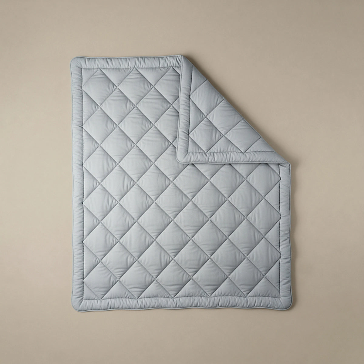 Eine hellgrau-blaue Steppdecke mit Rautenmuster - wie die Zelesta Royalbed Diamant - Grey-Blue, perfekt für Allergiker - liegt flach auf einem neutralen Hintergrund, wobei eine Ecke ordentlich umgeschlagen ist.