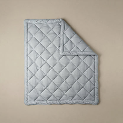 Eine hellgrau-blaue Steppdecke mit Rautenmuster - wie die Zelesta Royalbed Diamant - Grey-Blue, perfekt für Allergiker - liegt flach auf einem neutralen Hintergrund, wobei eine Ecke ordentlich umgeschlagen ist.