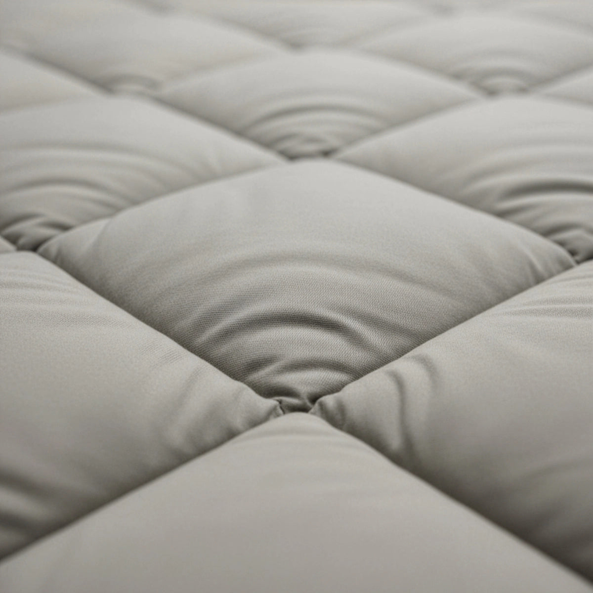 Nahaufnahme eines hellgrauen, gesteppten Stoffes mit gleichmäßig gepolsterten Quadraten und sichtbaren Nähten, die das temperaturregulierende Zelesta Royalbed Diamant - Sand-Beige zeigen, ideal als allergikergeeignete Bettdecke.