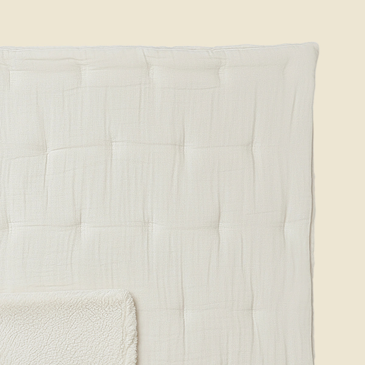 Eine Nahaufnahme der Zelesta Teddy Baumwolle Musselin - Beige, einer strukturierten, cremefarbenen Steppdecke mit quadratischem Muster und passender Fleecedecke, vor einem hellbeigen Hintergrund. Das temperaturregulierende Set sorgt für optimalen Komfort.