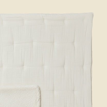 Eine Nahaufnahme der Zelesta Teddy Baumwolle Musselin - Beige, einer strukturierten, cremefarbenen Steppdecke mit quadratischem Muster und passender Fleecedecke, vor einem hellbeigen Hintergrund. Das temperaturregulierende Set sorgt für optimalen Komfort.