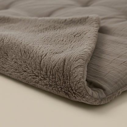Eine Nahaufnahme des Zelesta Teddy Baumwolle Musselin - Taupe zeigt seine weiche, gefaltete Textur mit einer Plüschseite und einer glatten, gesteppten Seite auf einer neutralen Oberfläche - perfekt für gemütliche Momente und temperaturregulierenden Komfort.