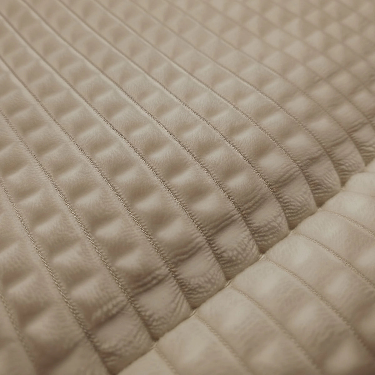Die Nahaufnahme von Zelesta Teddy Check - Taupe zeigt einen strukturierten beigen Stoff mit einem gesteppten, rechteckigen Muster und erhöhten, gepolsterten Abschnitten, die an eine Mikrofaser-Bettdecke erinnern.