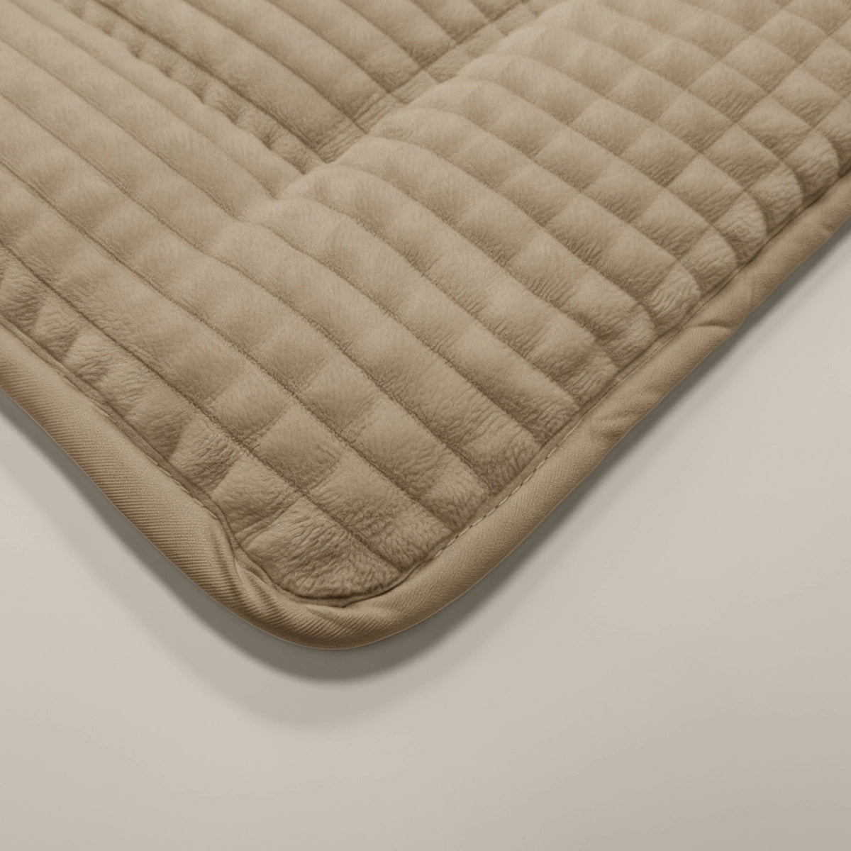 Nahaufnahme der Zelesta Teddy Check - Taupe, einer beigen, gesteppten Matte mit abgerundeten Ecken auf einer hellen Oberfläche. Sie hat ein gestreiftes, abgestepptes Muster für zusätzliche Struktur und Komfort.
