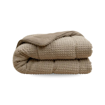 Eine gefaltete Zelesta Teddy Check - Taupe Mikrofaser Bettdecke mit Waffelstruktur und Steppmuster wird vor einem weißen Hintergrund präsentiert.
