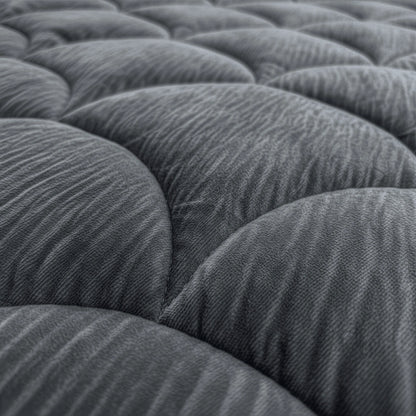 Nahaufnahme des Zelesta Flanel Velvetbed Chique - Anthrazit, mit einer grauen, gesteppten Oberfläche mit abgerundeten, gepolsterten Teilen, die ein sich wiederholendes Muster bilden.