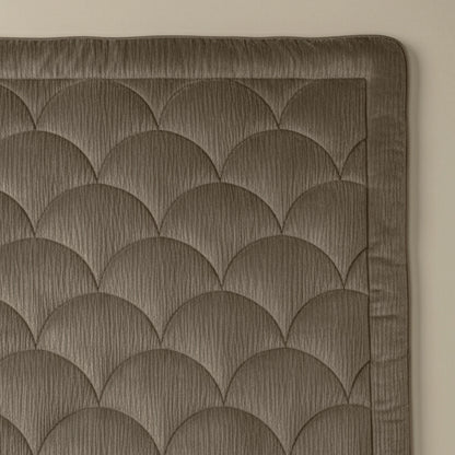 Nahaufnahme des Zelesta Flanel Velvetbed Chique - Taupe mit gestepptem Wellenmuster in gedämpftem Braun und unifarbener Umrandung vor einer hellbeigen Wand.