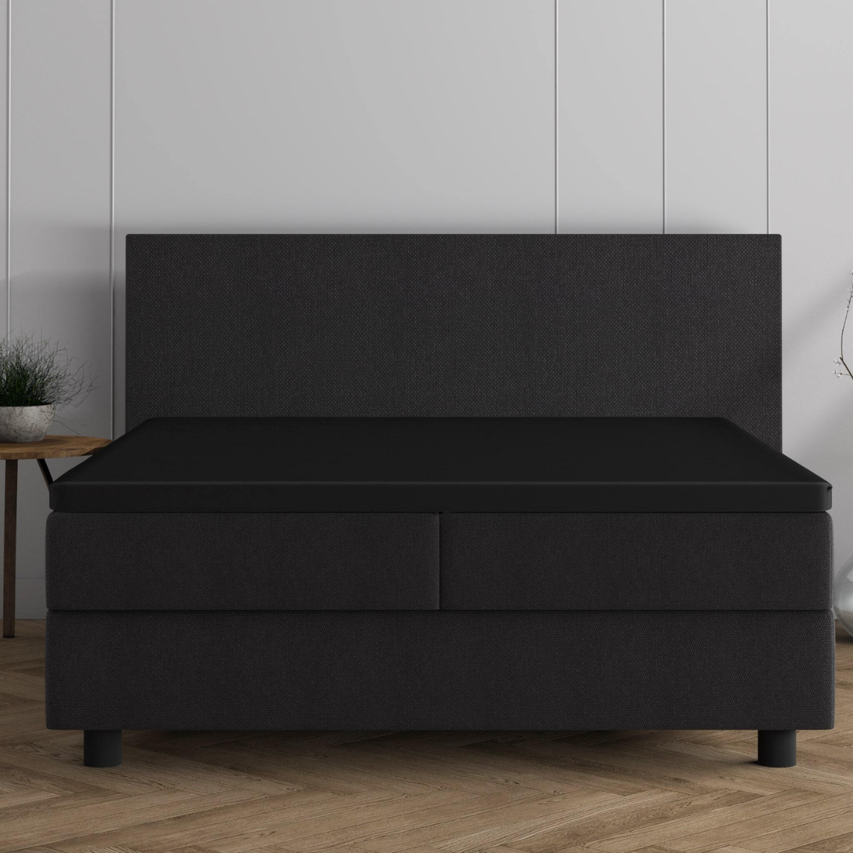 Ein modernes, dunkles Bett mit hohem Kopfteil und zwei Schubladen, bekleidet mit dem Doppel Jersey Topper Spannbettlaken - Schwarz, steht vor einer weiß getäfelten Wand auf einem Holzboden.